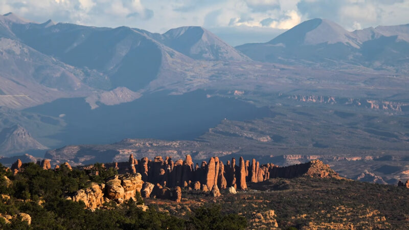 rock formations in Arches National Park, Utah, with distant mountain ranges under a partly cloudy sky