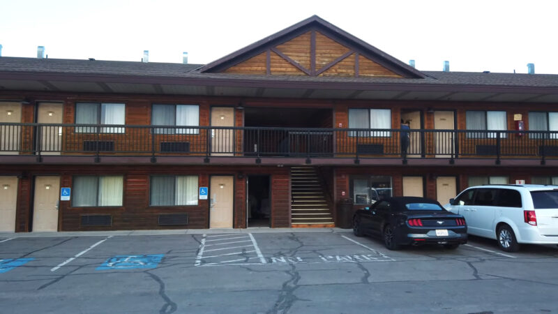 Exterior view of Best Western Plus Ruby's Inn featuring two levels of rooms, a wooden upper section, and a parking area with a black car and a white minivan in front