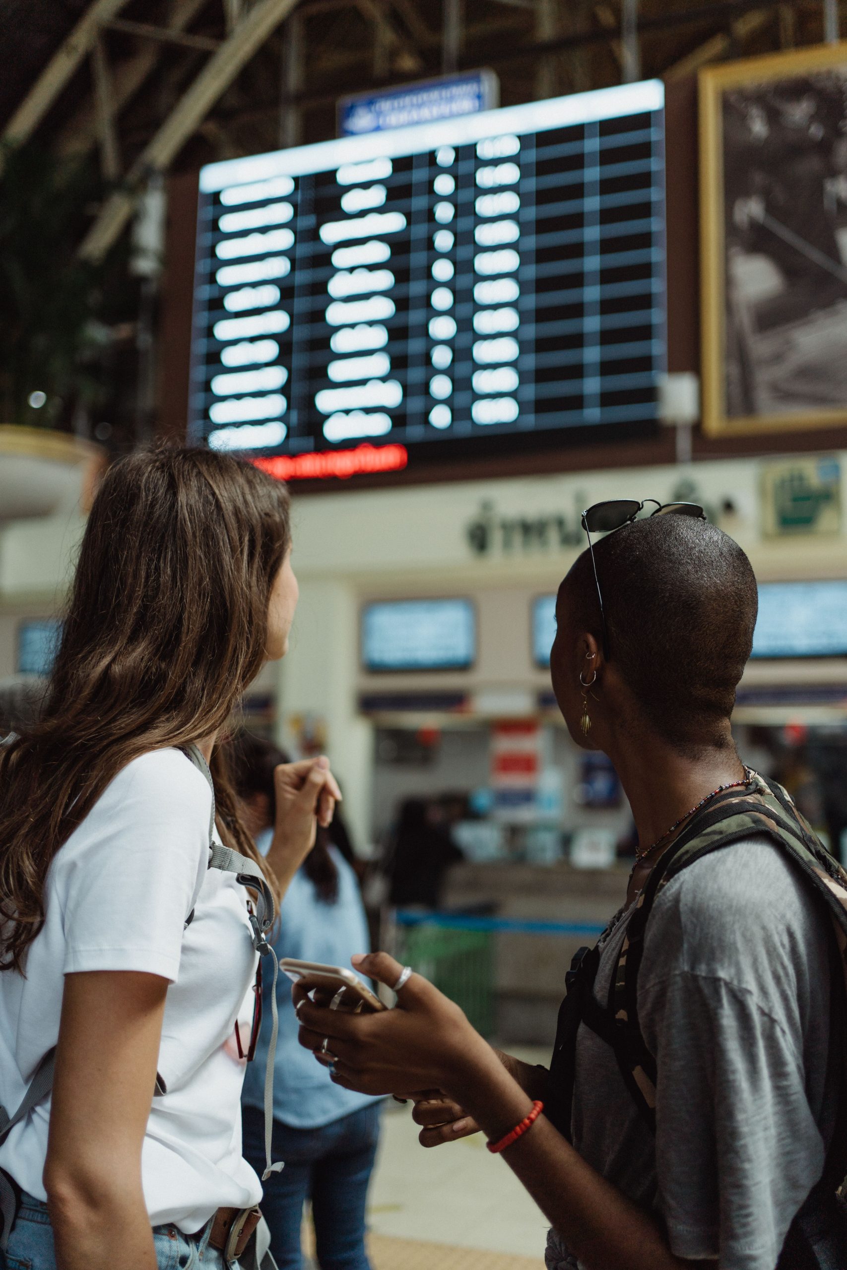 Two women checking the flight schedule on a departure board while traveling together